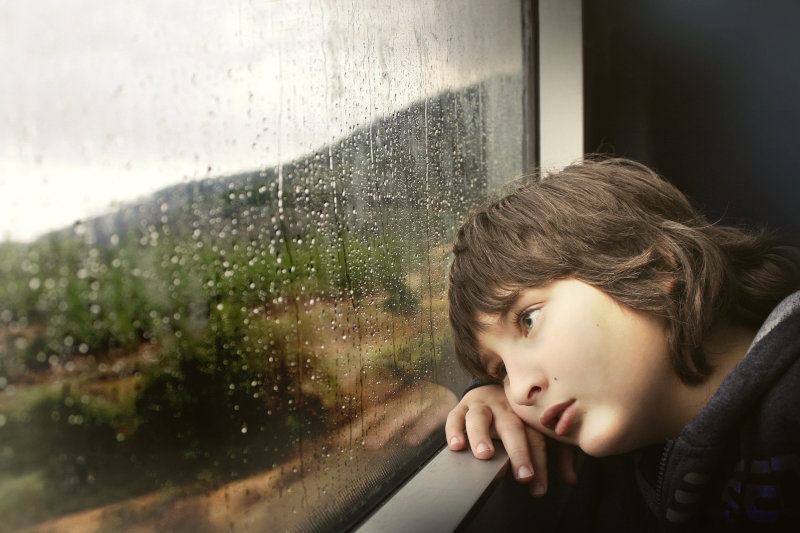 Kind schaut gelangweilt aus dem Fenster