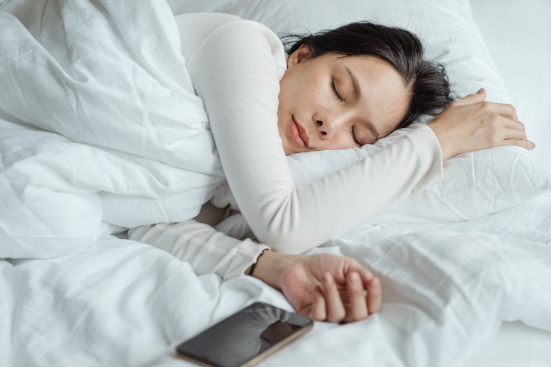 Frau im Bett mit einem Handy daneben