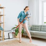 Frau reinigt glücklich ihre Wohnung mit einem Stausauger mit Wischfunktion