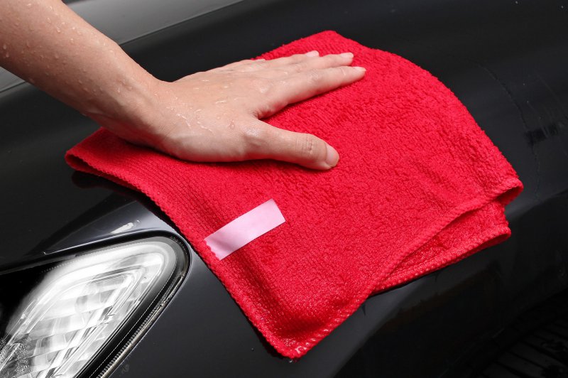 Eine Hand trocknet mit einem roten Mikrofasertuch das Auto.