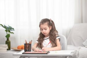 Kind sitzt auf einem Kinderschreibtischstuhl und macht Hausaufgaben