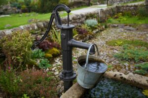Alte Hand- Wasserpumpe befördert Wasser in einem Sammelbecken